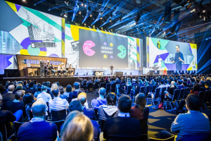 Eine große Menschenmenge sitzt auf Stühlen vor einer Bühne, einige Personen stehen auf dem Podium, ein Tisch mit Gegenständen links und Bildschirme und Lichter im Hintergrund auf der Deutschen Internet-Konferenz 2019.