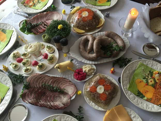 Ein für ein traditionelles deutsches Osteressen gedeckter Tisch mit verschiedenen Gerichten, Utensilien, Gläsern, Kerzen und Stühlen.