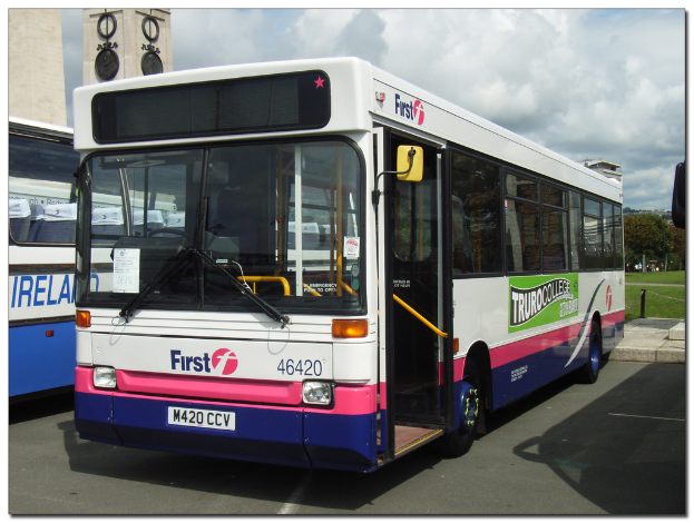 Eine Straße mit Bussen unten, ein Fußweg dahinter, Gras und Bäume in der Mitte und ein bewölkter Himmel oben.
