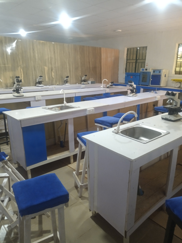 Ein Labor mit blauen Hockern, weißen Arbeitsplatten, einem Waschbecken mit Wasserhähnen, Maschinen, Fenstern an einer Wand und Deckenleuchten an der Universität für Wissenschaft und Technologie in Ahmedabad.