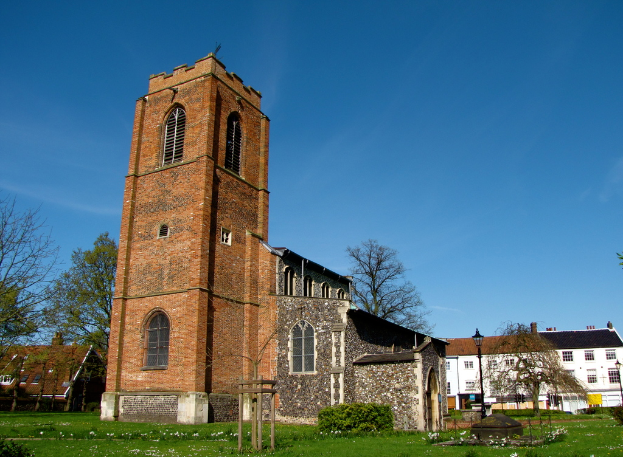 Ein grasbewachsener Bereich mit einem Mast, Gebäuden und Bäumen im Hintergrund.