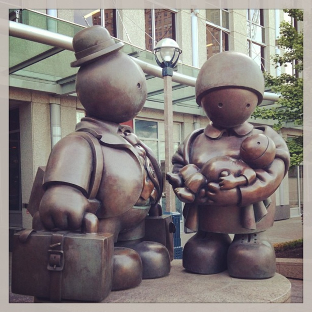 Skulpturen vor einem Gebäude mit einem Pfahl in der Mitte und einem Ast auf der rechten Seite.