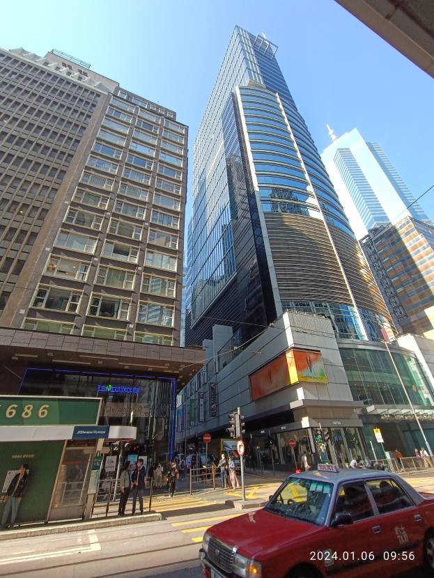 Ein rotes Auto fährt eine von hohen Wolkenkratzern gesäumte Stadtstraße entlang, mit Passanten, Verkehrsampeln und verschiedenen Schildern.