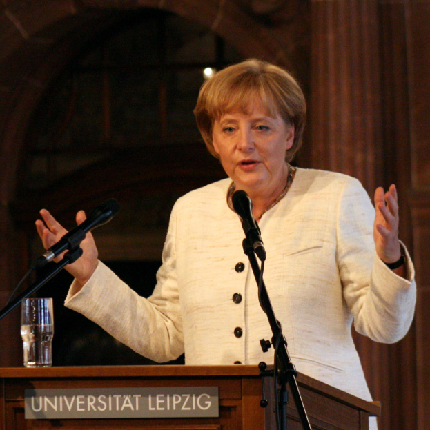 Bundeskanzlerin Angela Merkel hält eine Rede an der Universität Leipzig und steht dabei an einem Rednerpult mit einem Mikrofon und einem Glas Wasser.