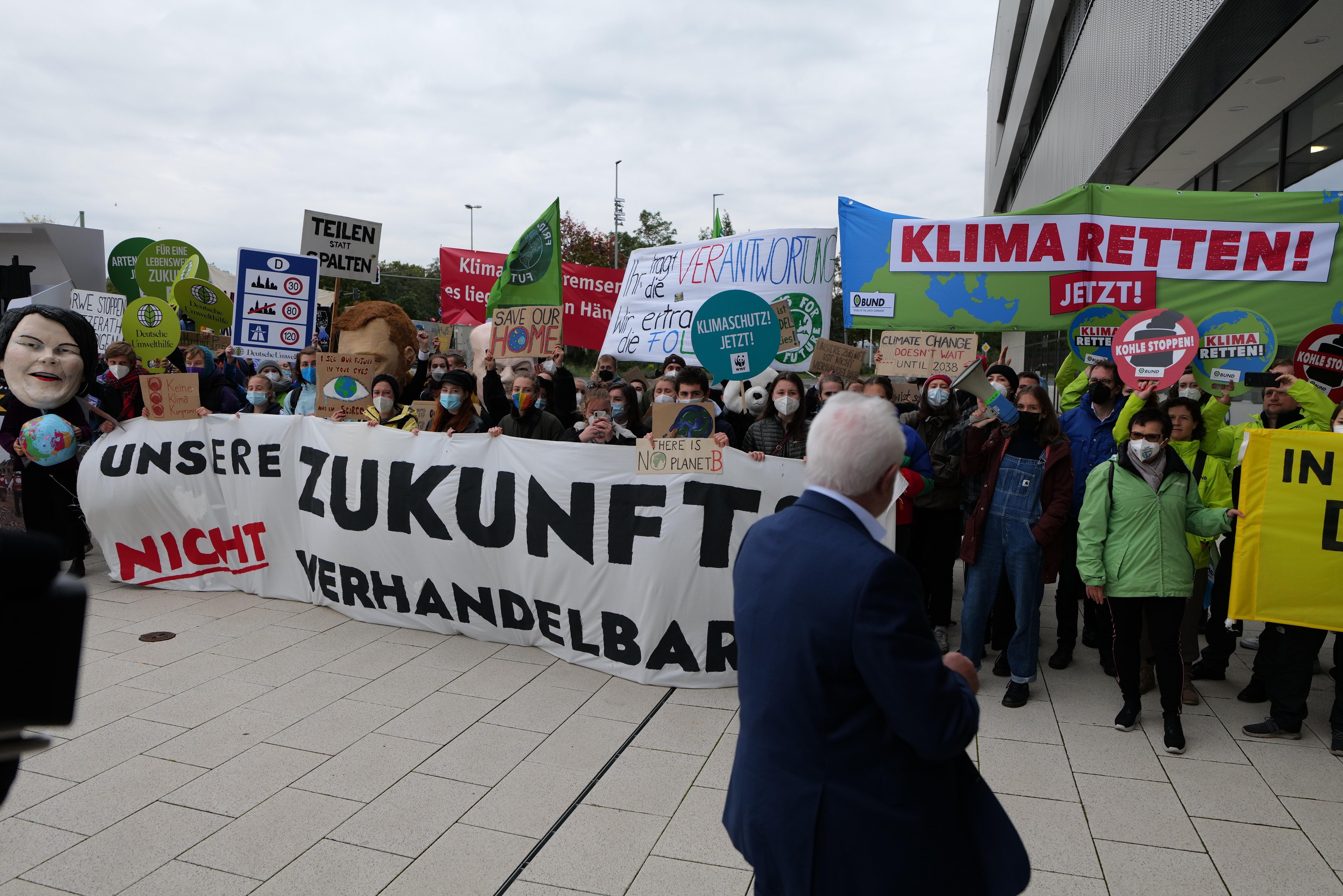 Eine Gruppe von Menschen protestiert gegen den Klimawandel in Deutschland, sie halten Schilder und Banner vor einem Gebäude, während ein Fotograf das Ereignis dokumentiert.