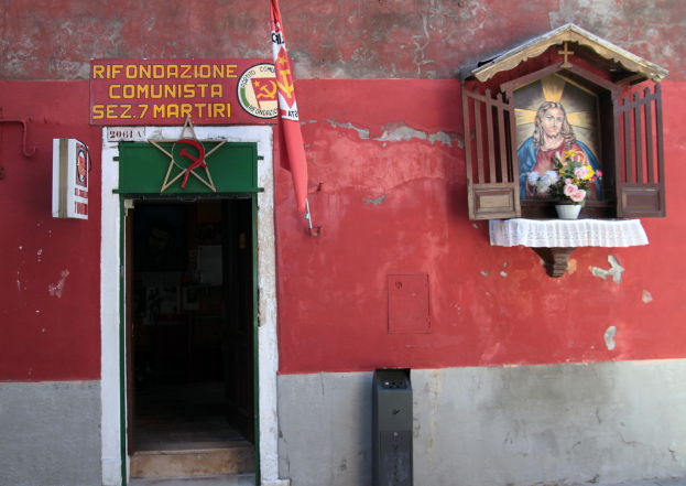 Ein rotes Gebäude mit einer roten Flagge, ein Jesus-Foto und ein Blumentopf auf einem Holzregal, mit Text an der Wand.