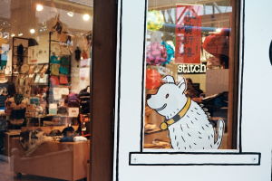 Eine Illustration eines Hundes mit Text auf der rechten Seite und links ein Raum mit Lichtern, Flaggen, Regalen, Sofas, Kleidung, Dekorationen, Menschen, Stühlen und verschiedenen anderen Gegenständen.