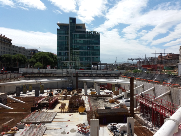 Baustelle mit einem großen Gebäude im Hintergrund, umgeben von Bäumen, Pfählen, Lampen und anderen Gegenständen unter einem bewölkten Himmel, als Europäischer Union Hauptsitz identifiziert.
