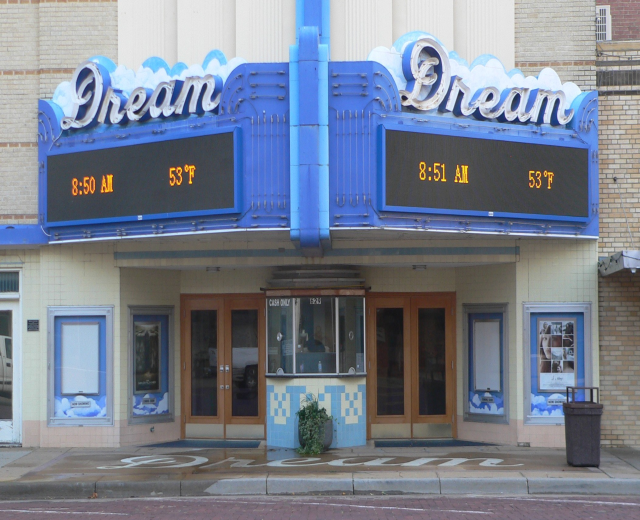 Außenansicht des Dream Theaters in St. Louis, Missouri, mit Glasfenstern und -türen, einer Schautafel, einem Müllcontainer, einem Topfpflanze und einer Straße unten.