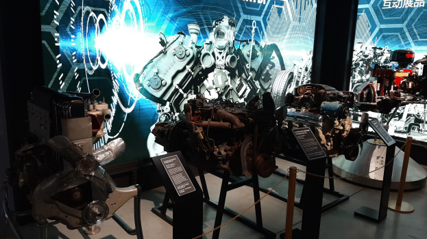 Ein Raum voller verschiedener Motorenarten, die ausgestellt sind, mit Maschinen auf Ständern und Texttafeln im Hintergrund, mit einem prominenten Rad.