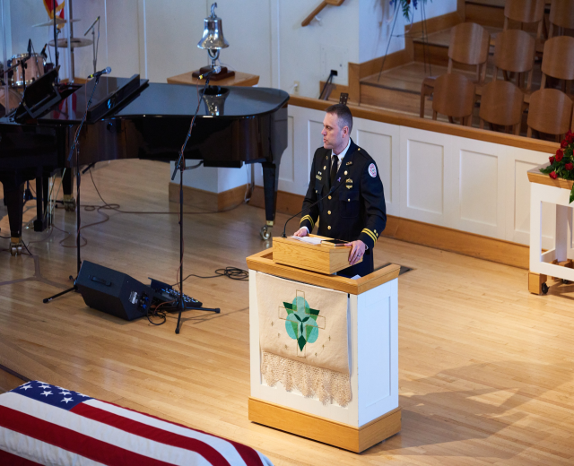 Polizeibeamter mit Mikrofon an einem Rednerpult vor einem Klavier und diverser Eventausstattung