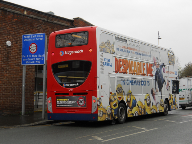 Ein weißer und roter Bus steht auf einer Straße mit einer roten Backsteinwand und einem blauen Warnschild im Hintergrund.