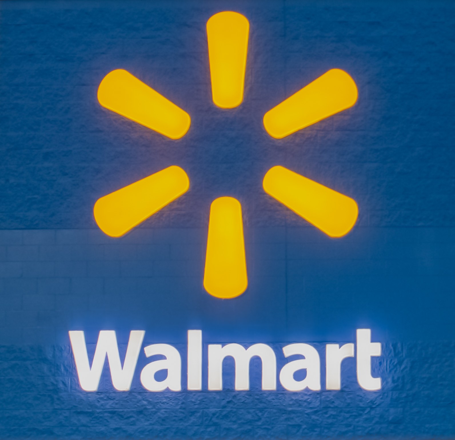 Blaue Wand mit dem Walmart-Logo in weißer Schrift, beleuchtet von hellem gelbem Licht.