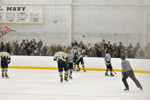 Eine Gruppe von Menschen, die Eishockey auf einem Eisplatz spielen, tragen Helme und halten Hockey-Schläger, mit Zuschauern auf den Tribünen und einem Banner an der Wand im Hintergrund.
