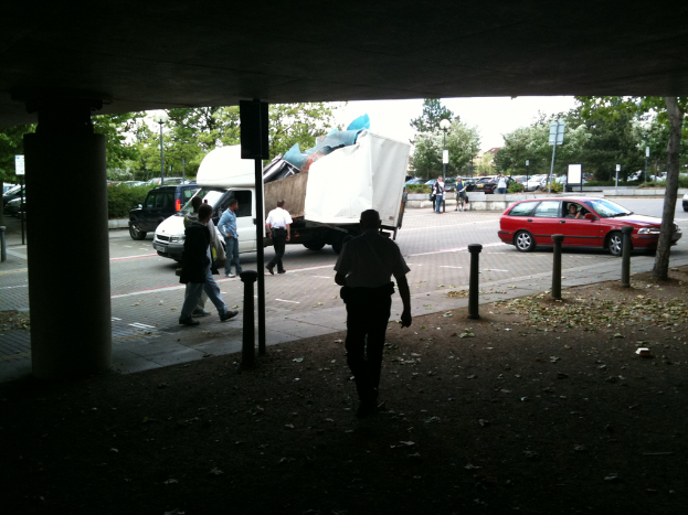 Eine belebte Straßenszene mit zahlreichen Fußgängern, einem Auto und einem Lastwagen auf der Straße.