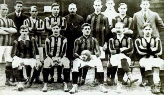 Schwarzes und weißes Foto einer Fußballmannschaft, einige stehen, einige sitzen, vor einer Wand mit dem Text "Ballymena Football Club" unten.