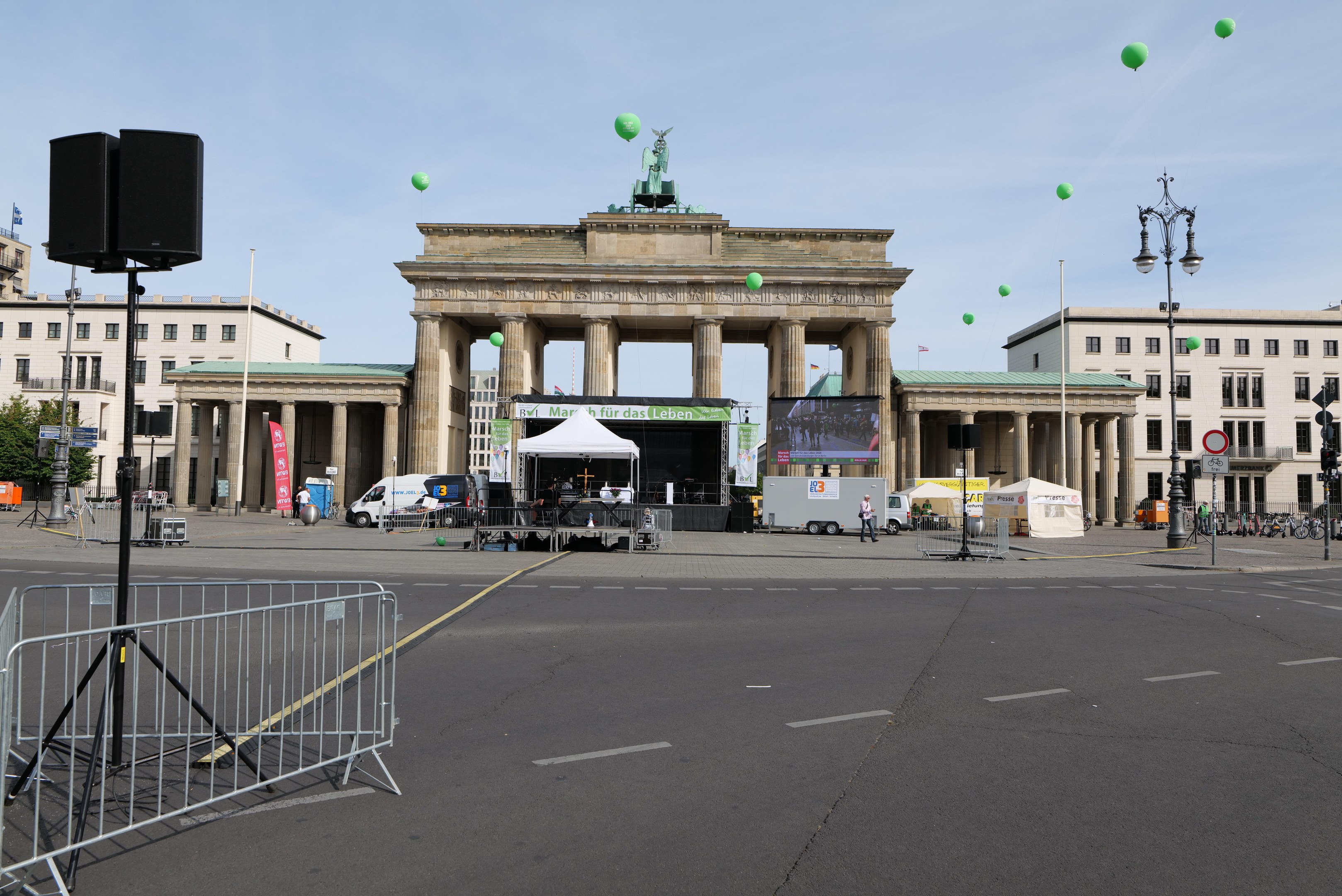 Das Brandenburg-Tor in Berlin, Deutschland, mit festlichen grünen Luftballons am bewölkten Himmel während des Berlin-Marathons, umgeben von Gebäuden, Laternenmasten, Ampeln, Zelten, Fahrzeugen, Menschen und Fahrrädern.
