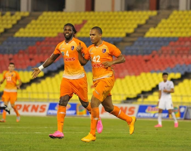 Eine Gruppe von Männern in den Farben der Indian Super League (IPL) 2019-20, die auf einem Rasenfeld Fußball spielen, mit Werbetafeln, Stühlen, Säulen und Wänden im Hintergrund.