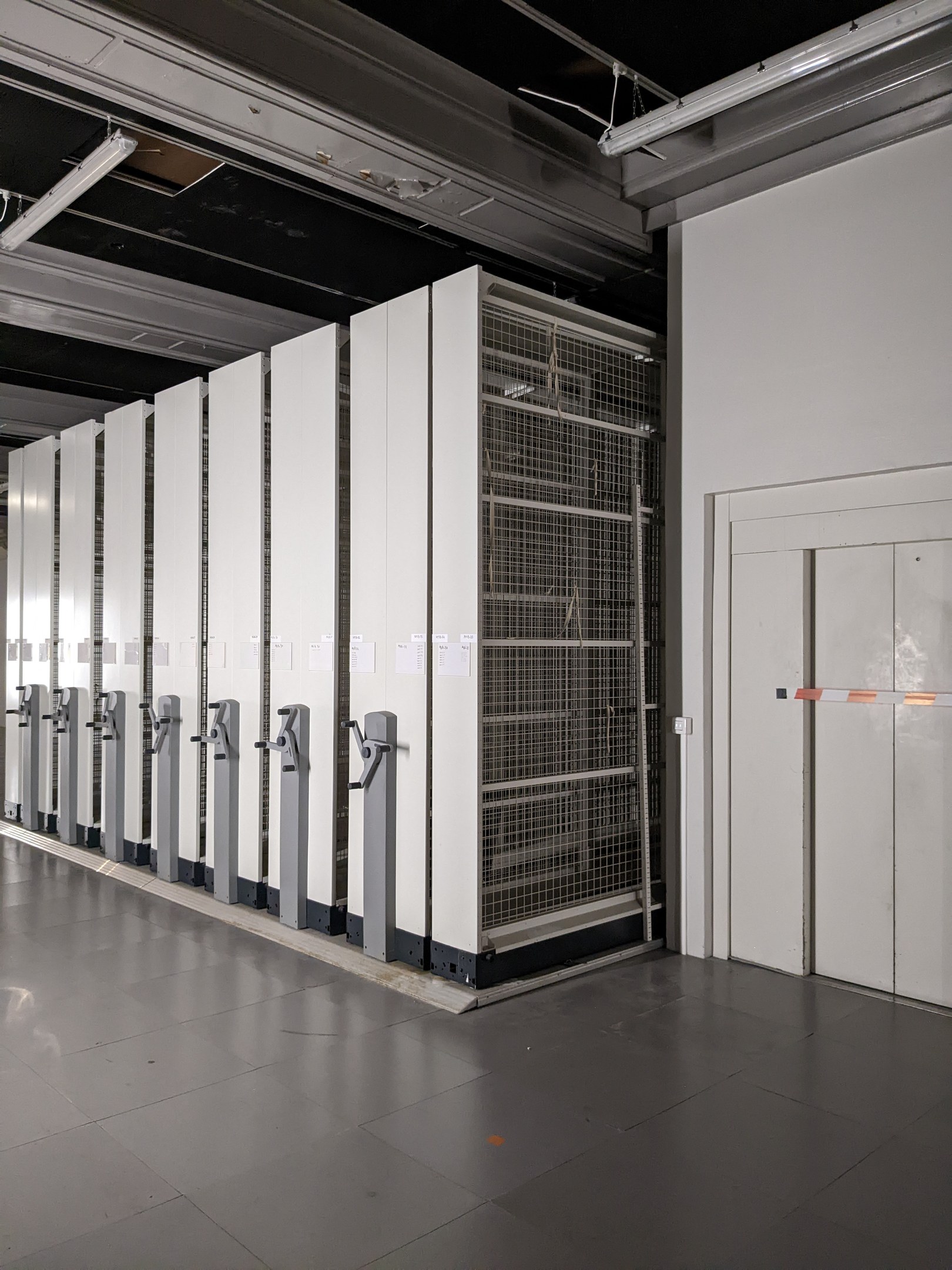 Ein gro├če Rechenzentrumsraum mit zahlreichen Servern, mit einem Boden, einer rechten Wand und einer Decke mit Beleuchtung überkopf.