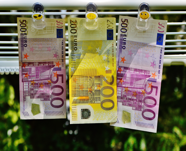 Drei Euro-Banknoten an einer Wäscheleine mit Klammern, vor einem unscharfen Hintergrund.