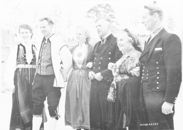 Ein Schwarz-Weiß-Foto einer Gruppe von Menschen, die draußen zusammenstehen und lächeln, mit Bäumen im Hintergrund und dem Text "Bayerische Familie in den 1930er Jahren" unten.