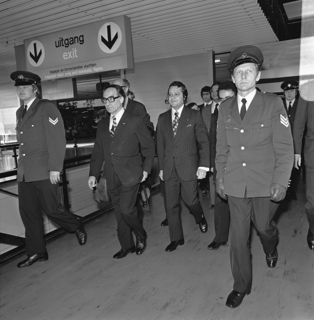 Schwarzes und weißes Foto einer Gruppe uniformierter Männer, die durch einen Flughafen gehen, mit einem Schild an der Wand im Hintergrund.