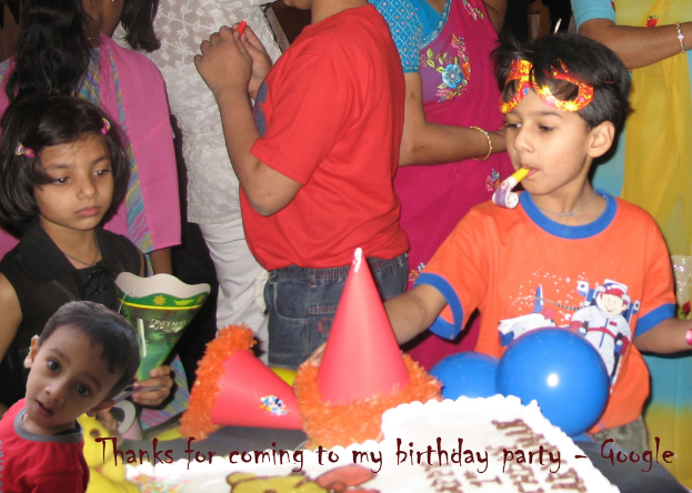 Kinder stehen vor einem Tisch mit einem Kuchen, Luftballons und Mützen, mit anderen Menschen im Hintergrund.