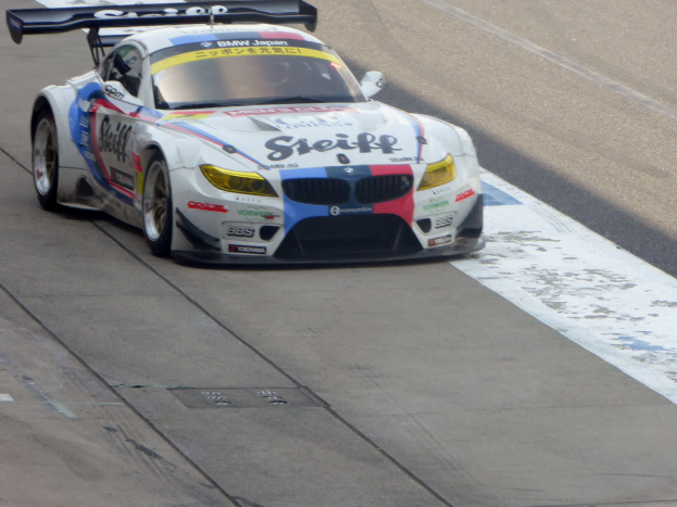 Ein strahlend blauer und weißer BMW Z4 GT3 Rennauto mit großen glänzenden Rädern fährt auf einer Rennstrecke und präsentiert seine aerodynamische Form und niedrige Profilierung.