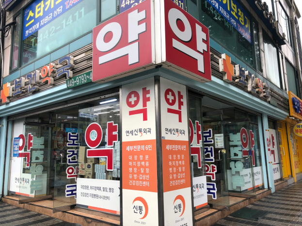 Ein Gebäude mit Glaswänden und -türen, das Schilder mit der Aufschrift "Südkoreas erste Apotheke in Seoul, Südkorea" und ein Schild an der Seite trägt.