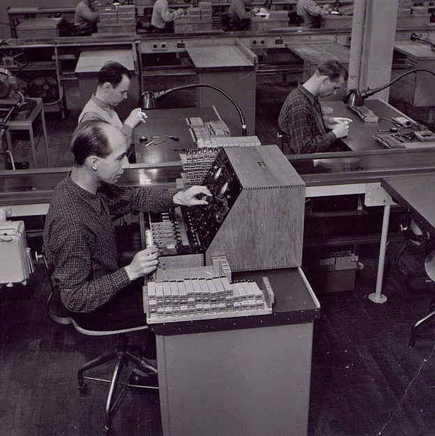 Schwarz-weißes Bild von Männern, die an Fabriklernplätzen arbeiten.