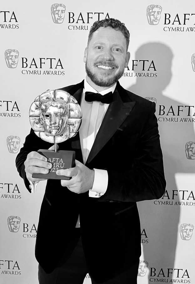 Ein Mann im Smoking mit einem BAFTA-Award, der vor einer Tafel mit 'BAFTA Awards 2018' steht.
