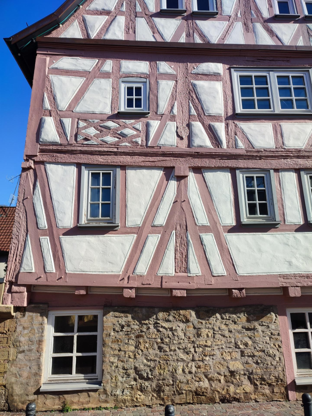 Ein Fachwerkhaus in Rothenburg ob der Tauber, Deutschland, mit pink-weißer Fassade, mehreren Fenstern und einem blauen Himmel im Hintergrund.