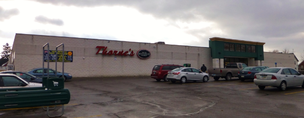 Ein bewölkter Himmel mit einer Wand und Brettern auf der linken Seite und Fahrzeugen einschließlich eines Wagens auf der Straße auf beiden Seiten.
