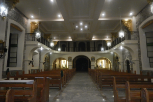 Das Innere einer Kirche mit hölzernen Kirchenbänken, Tischen in der Mitte, Geländern, Lampen und Skulpturen, mit detaillierten Verzierungen an den Wänden und einer warm beleuchteten Decke.