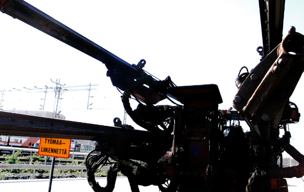 Eine Maschine ist im Vordergrund zu sehen, im Hintergrund sind Strommasten, Kabel, Absperrungen, Pflanzen und Himmel zu erkennen.