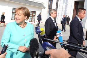 Bundeskanzlerin Angela Merkel spricht mit Reportern vor dem Kanzleramt in Berlin umgeben von Menschen mit Mikrofonen und Gebäuden im Hintergrund.