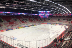 Ein Eishockeyspiel in einer grossen Arena mit Zuschauern, einem Zaun um die Eisbahn, einem Display mit der Aufschrift "St. Louis Blues vs Detroit Red Wings", Metallrahmen und einer Decke mit Deckenleuchten.