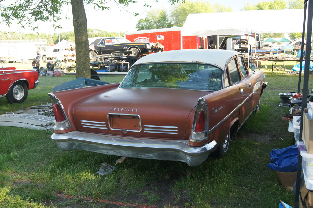 Autos auf dem Rasen mit Bäumen, Tischen mit Gegenständen und einer Hütte im Hintergrund.