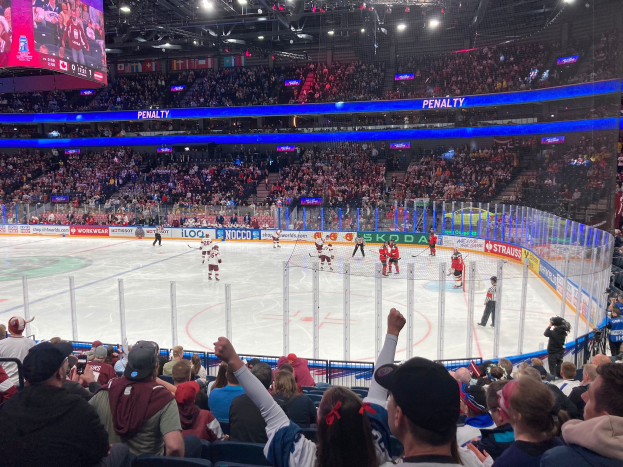 Ein Eishockeyspiel in einer großen Arena mit Zuschauern auf den Rängen, eine Eisfläche umgeben von einem Zaun, ein Kameramann auf der rechten Seite und ein Bildschirm mit der Anzeige 'Tulsa SunTrust Center Section 103 Row A Seat 1' oben.