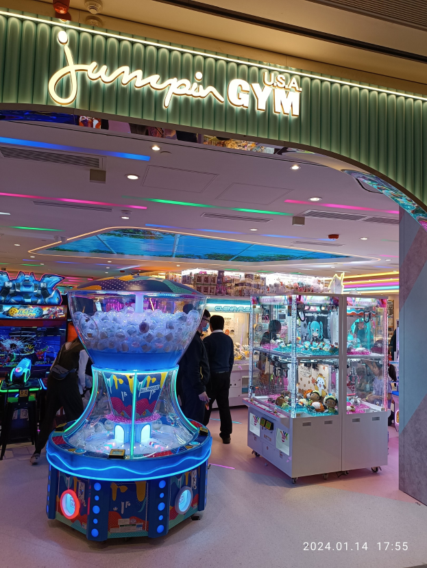 Gruppe von Menschen vor einem hell erleuchteten Jumpin' USA Gym im Mall of Asia mit bunten Arcade-Maschinen, einem Namensschild oben und einem Wasserzeichen in der rechten unteren Ecke.