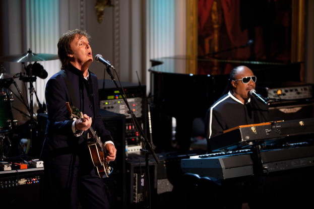 Paul McCartney und Stevie Wonder performen gemeinsam bei den Grammys, wobei McCartney Gitarre spielt und singt und Wonder eine Brille trägt, während er am Piano spielt.