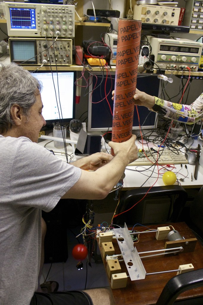 Ein Arbeitsplatz mit Maschinen, Kabeln, einem Computerbildschirm, einem Kugelschreiberhalter, Menschen und einem Stressball.