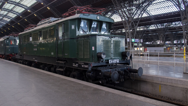 Ein Zug auf Schienen mit Geländern und Brettern im Hintergrund, Lichter auf dem Dach und ein Himmel darüber, mit einem Boden und Schienen darunter.
