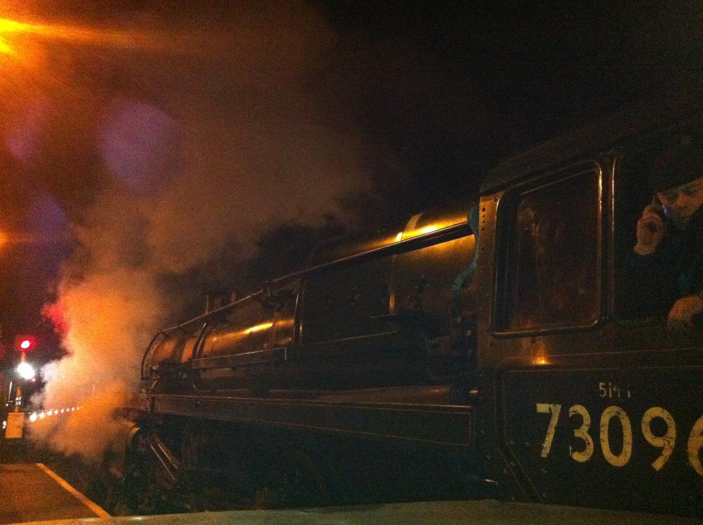 Ein Dampflokomotive-Zug auf Eisenbahnschienen unter einem dunklen Himmel.