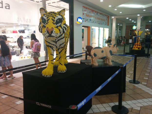 Statuen von Tieren auf schwarzen Kisten umgeben von Pfählen mit Gummigürteln, mit Geschäften, die Taschen, Schuhe und andere Artikel anbieten, und Menschen, die herumlaufen.