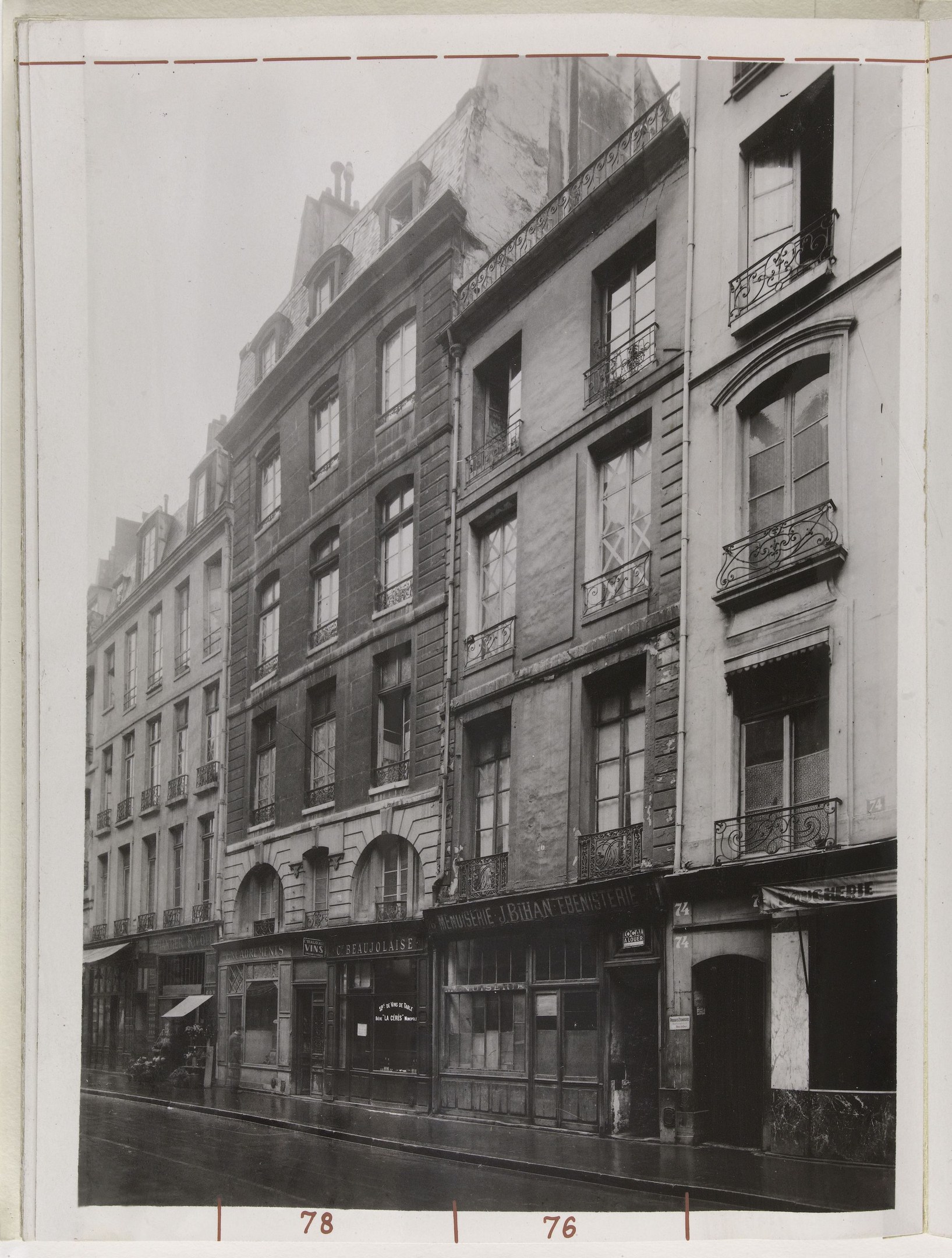 Schwarzes und weißes Foto einer Stadtstraße mit Gebäuden, Fenstern, Geländern, Namensschildern und einer Straße unten.