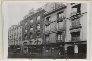 Schwarzes und weißes Foto einer Stadtstraße mit Gebäuden, Fenstern, Geländern, Namensschildern und einer Straße unten.