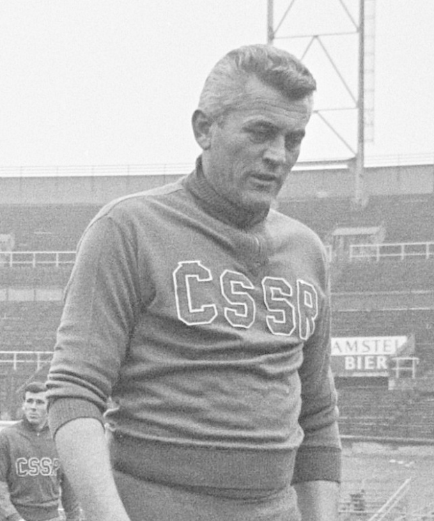 Ein Schwarz-Wei√ü-Foto eines Mannes, der in einem Feld steht und ein T-Shirt mit Text tr√§gt, vor einem Stadion und einer Werbetafel, vermutlich der F√ľrballspieler Cesar Azpilicueta.