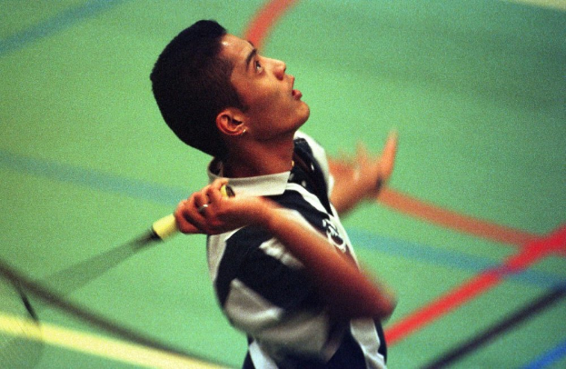 Ein junger Mann spielt Badminton auf einem Court und hält einen Schläger in der Hand, mit entschlossener Miene.