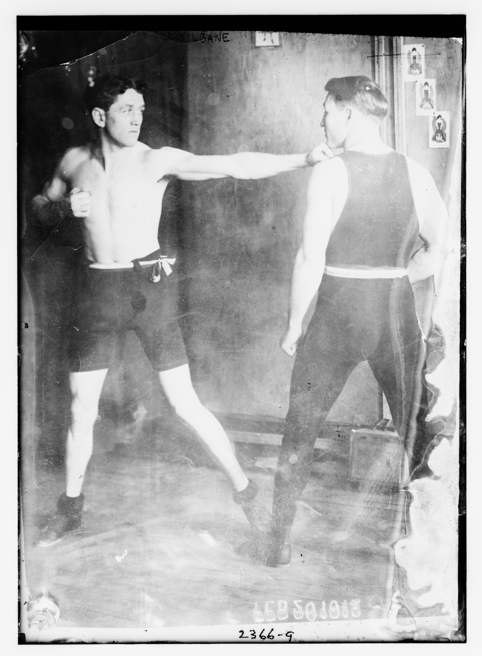 Schwarzes und wei├čes Foto von zwei Boxern in einem Boxring mit Postern an der Hintergrundwand und Text unten.